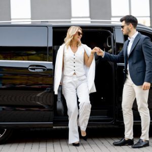 A man helps a woman exit a black vehicle, showcasing elegance and courtesy.
