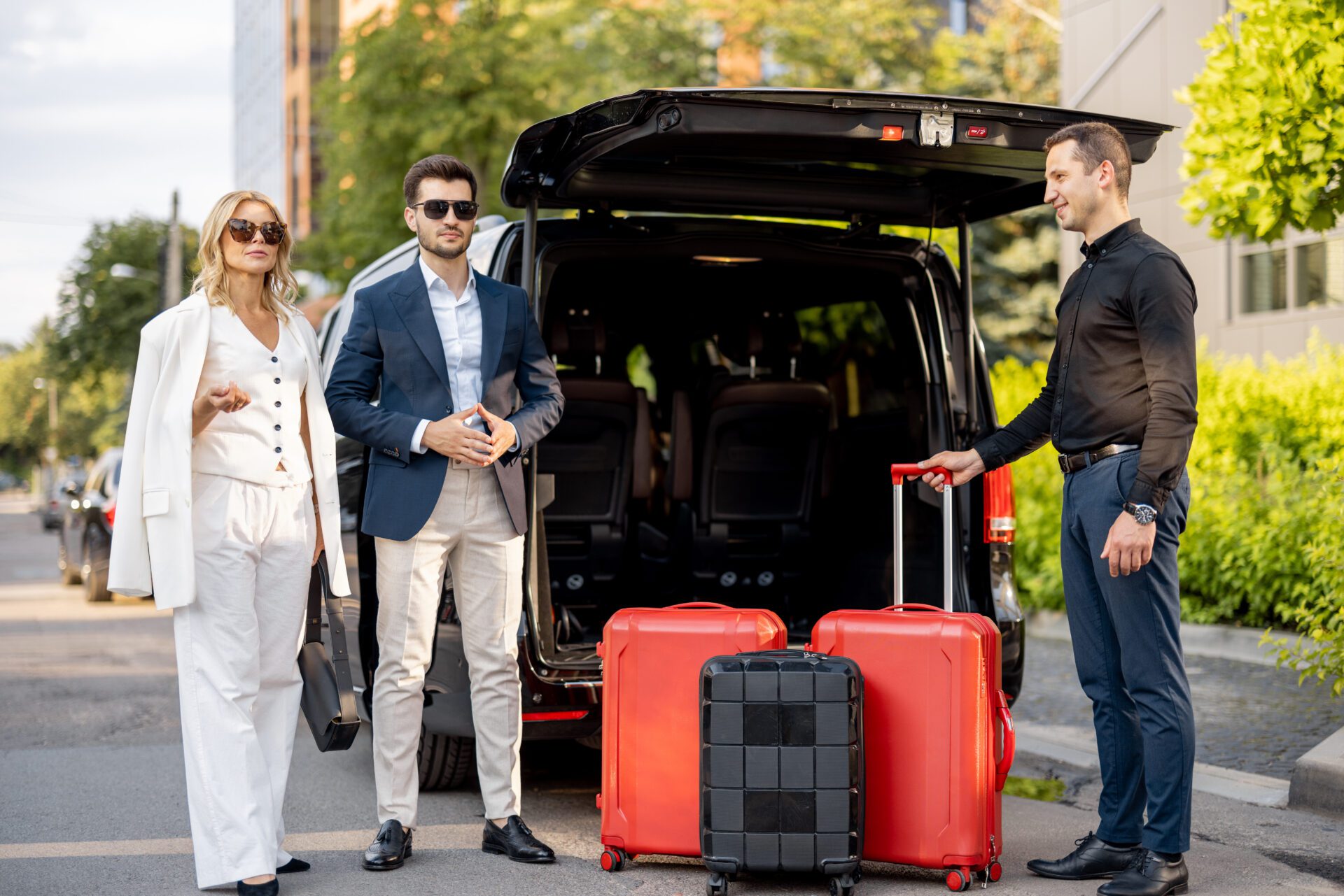 Three stylish travelers with red luggage near a black SUV in a sunny setting.