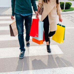 Two people walking with colorful shopping bags across a crosswalk.